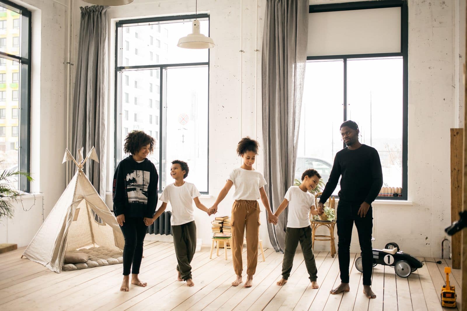 A Black father and four children holding hands in a bright family home