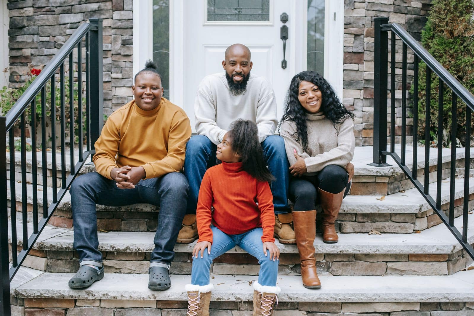 A young Black family sitting together on the front steps of their home